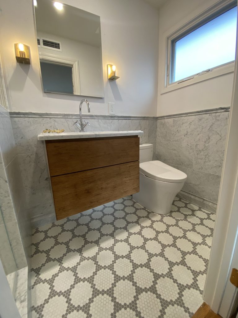 Bathroom with a floating wood vanity, wall sconces and a hexagonal tile floor
